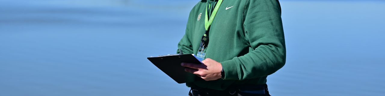 inspector taking notes on a clipboard with a lake in background